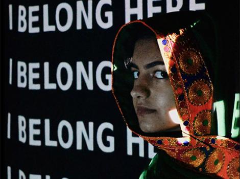 young Muslim woman in front of a projection of I Belong Here