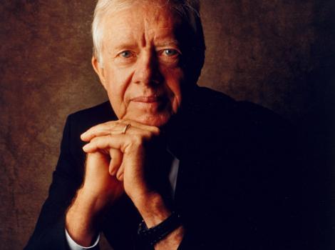 Photographic portrait of President James Carter sitting with his elbows on his knees and head on folded hands. 