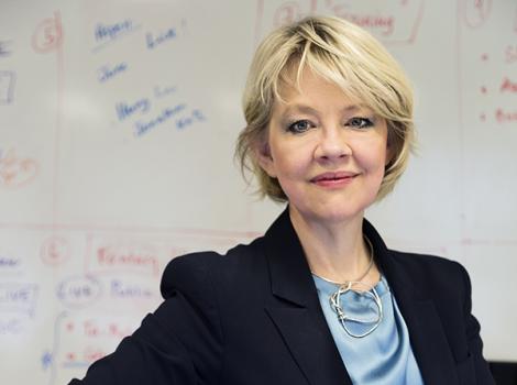 Blond woman with blue eyes wearing a blue blouse and black blazer
