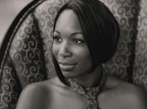 Venus Williams sits in a chair wearing a dress and smiling and looking to her right.
